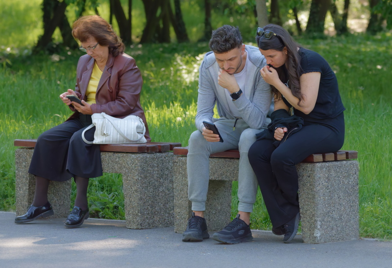 People with smartphones on a park bench